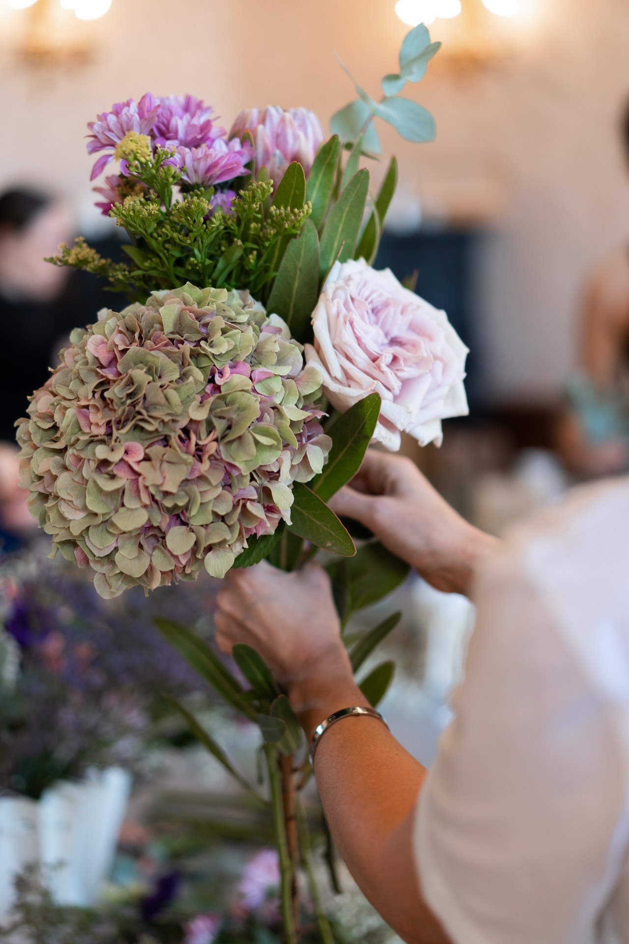 Hands arranging a single white garden rose into a soft bouquet